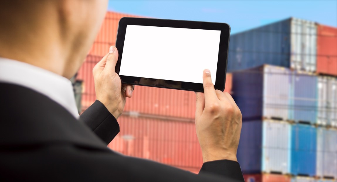 Businessman surfing of a digital tablet and reviewing a tack of shipping containers